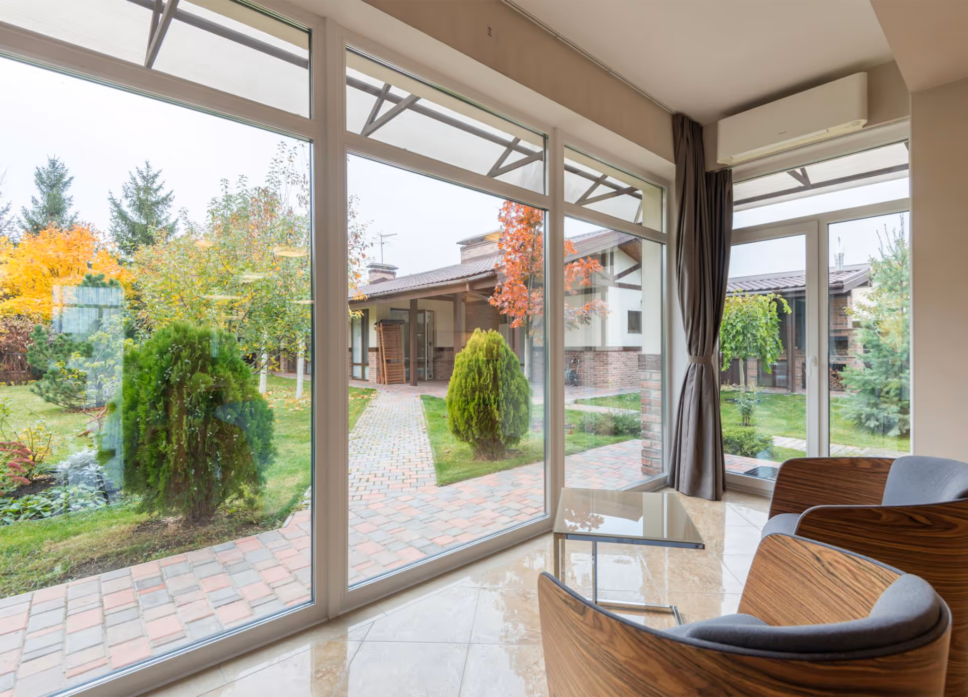 A modern living space with wall to wall, floor to ceiling windows looking out on to a lush garden.