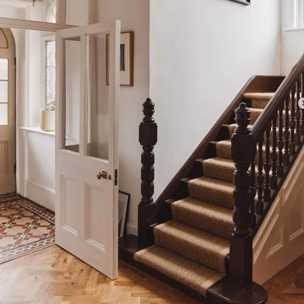 A hallway in a period home with a wooden staircase and natural sisal stair runner.