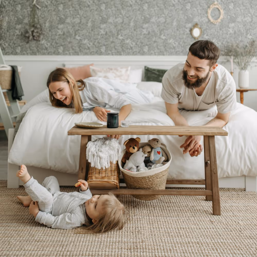 A couple watching their young child playing on a natural fibre carpet.