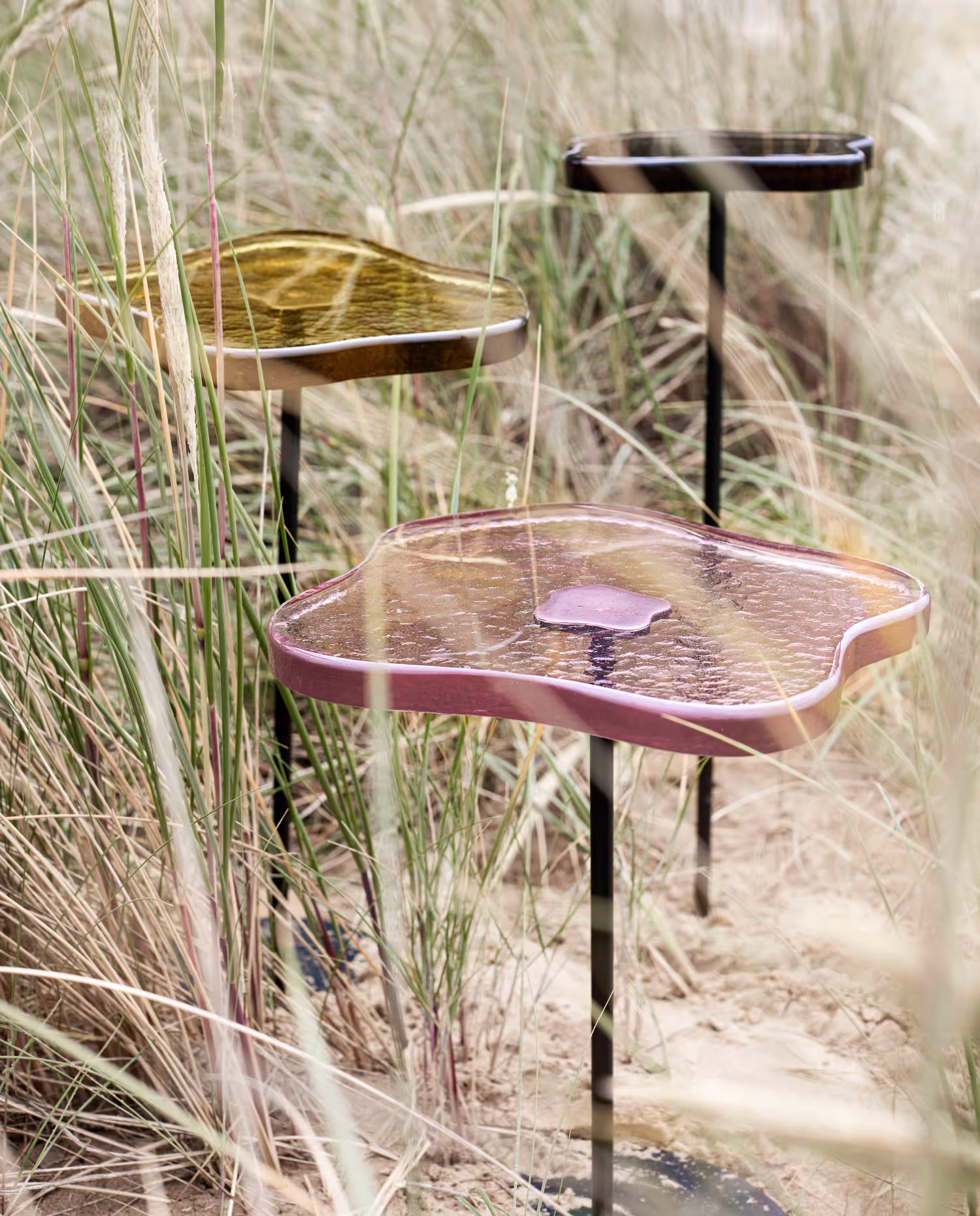 Three glass topped metal cocktail tables displayed in a sand dune.