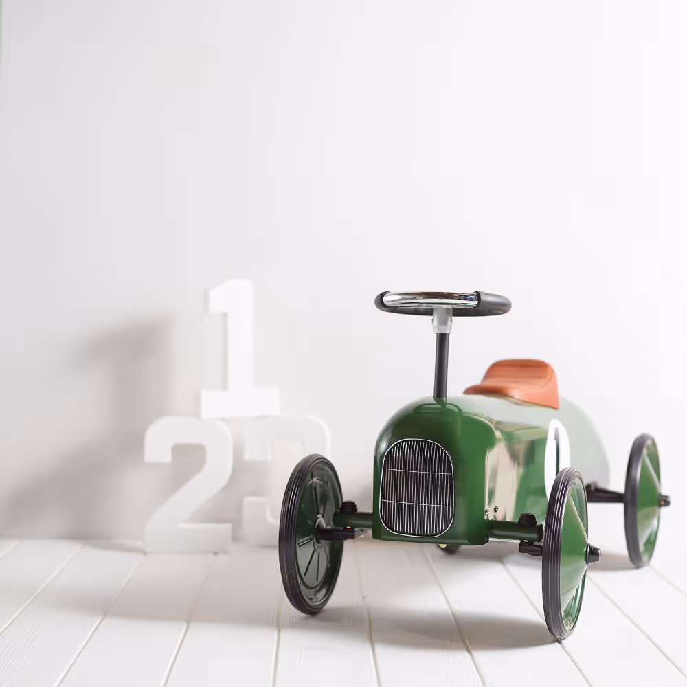 A white painted wall with white painted floorboards and a vintage green kids pedal car.