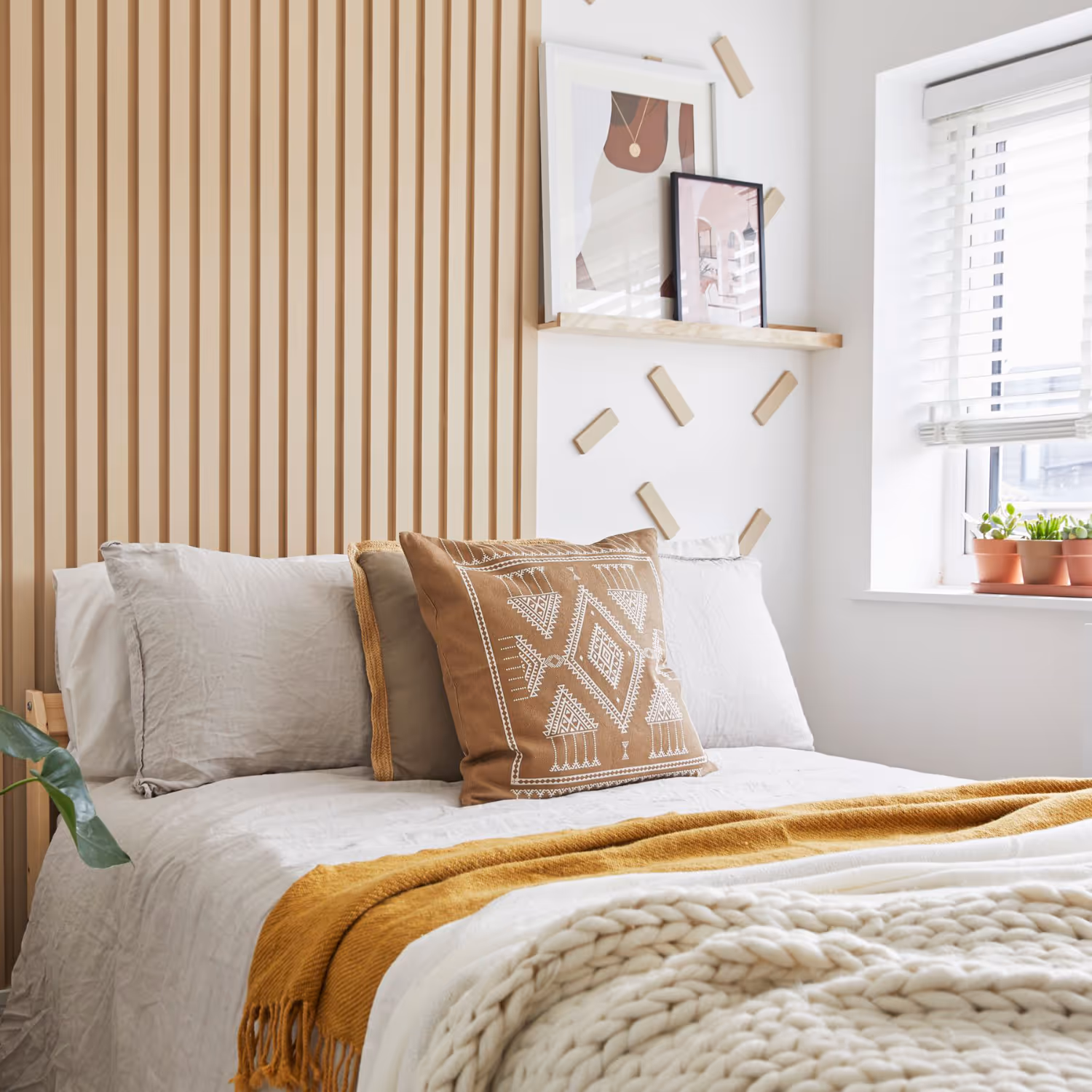 A biophilic designed bedroom in neutral tones with natural wood panelling, linen bedding and a mustard throw.