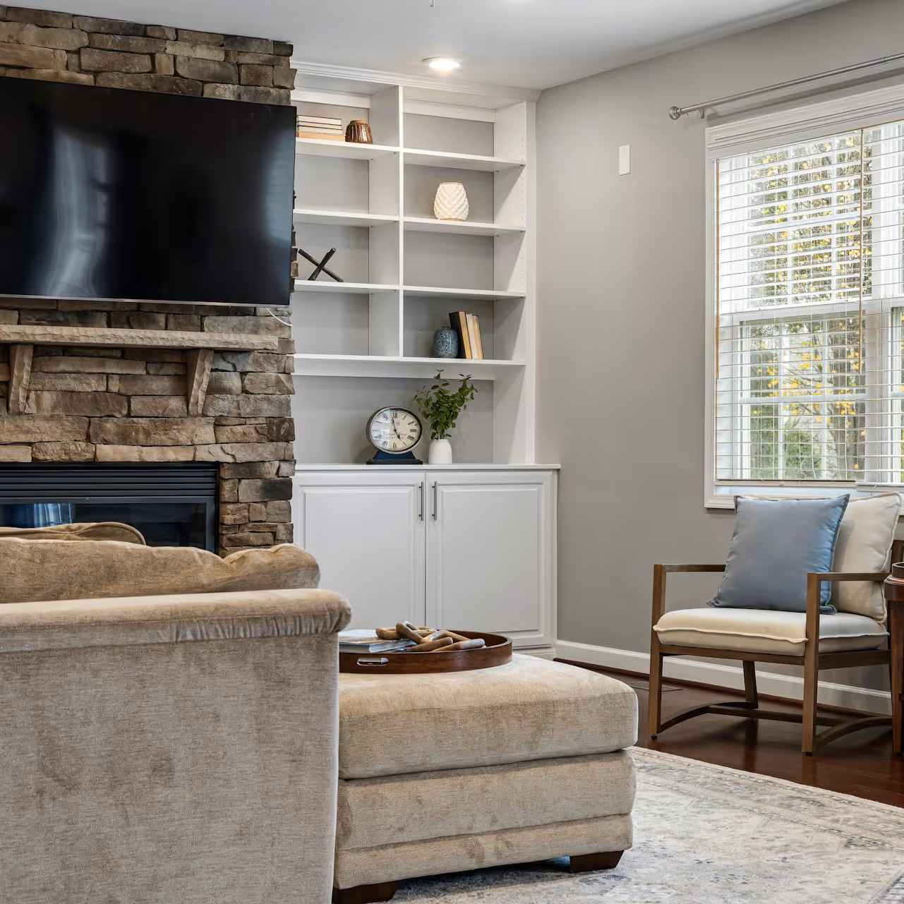 A living room with neutral decor and an exposed stone fireplace.