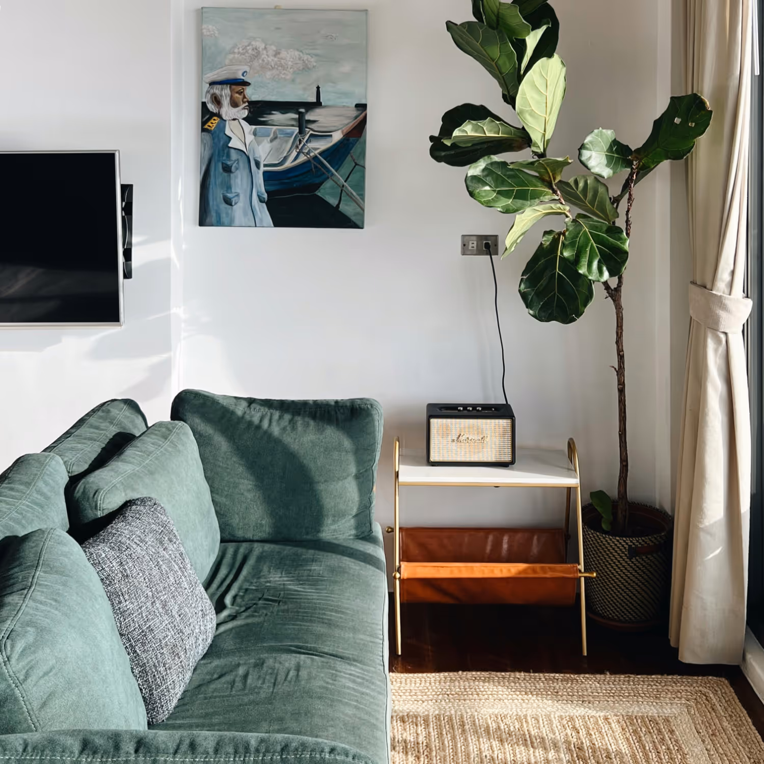 A biophilic designed living room with a sea green velvet sofa, seagrass rug, neutral walls and a lush green potted plant.