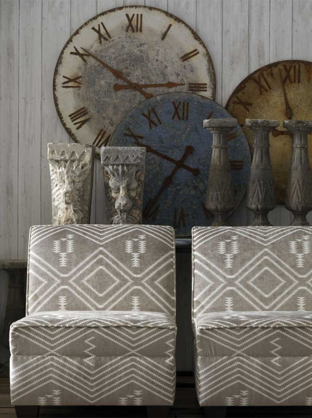 Two simple upholstered chairs in front of a console table adorned with driftwood accessories and a wall decorated in a timber tongue and groove pattern wallpaper.