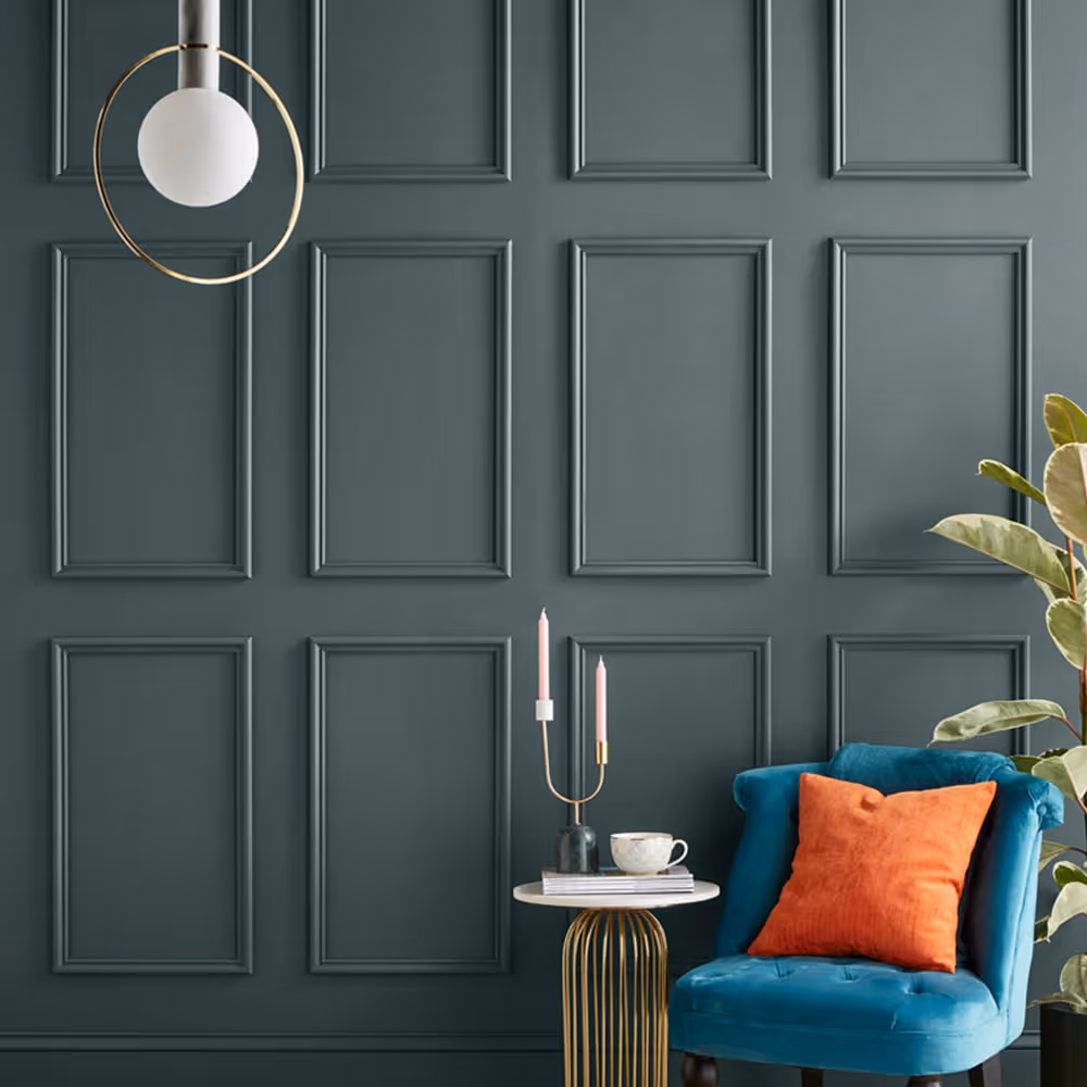 A dark teal panelled wall with a teal occasional chair and gold side table
