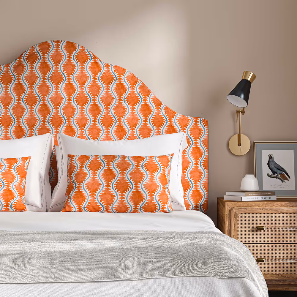 A bed with a large headboard upholstered in an orange printed linen, with matching cushions and white bedlinen.
