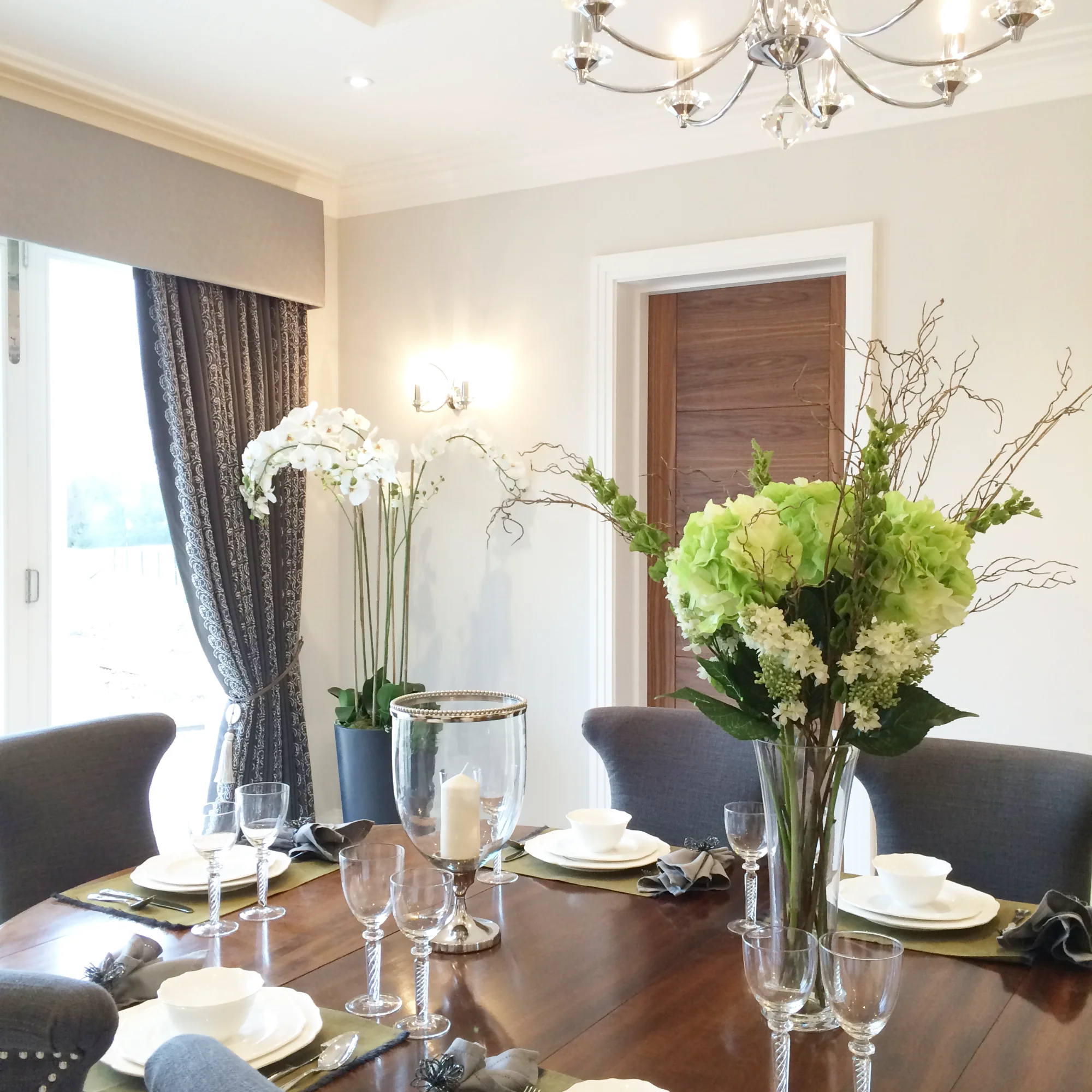 A dining room with neutral walls and a large antique walnut dining chair with contemporary grey upholstered chairs.