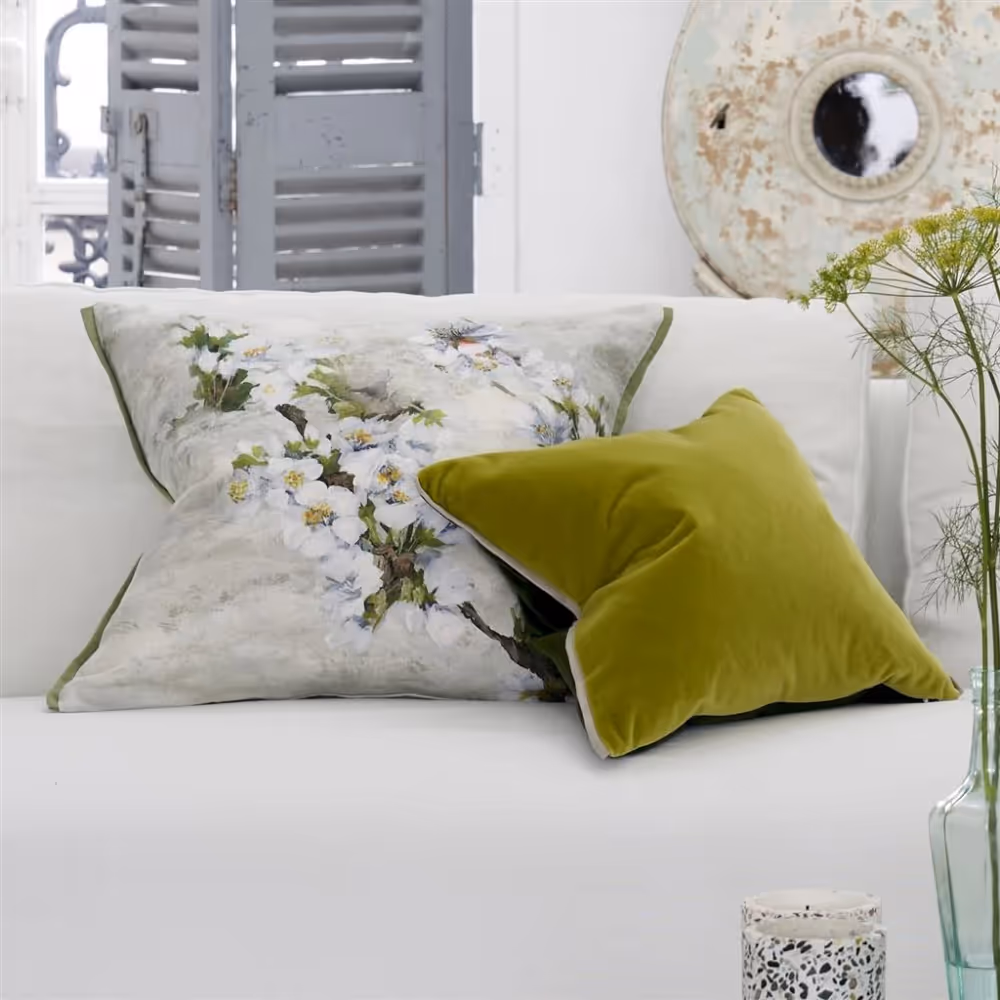A green cushion and a white and grey floral cushions on a white linen sofa.