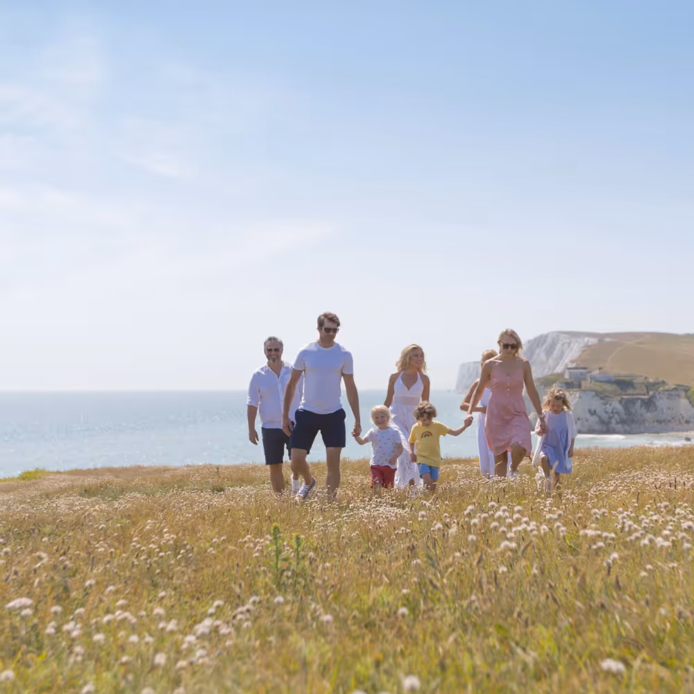 A family enjoying a cliff top walk with a view of a stunning bay behind them.