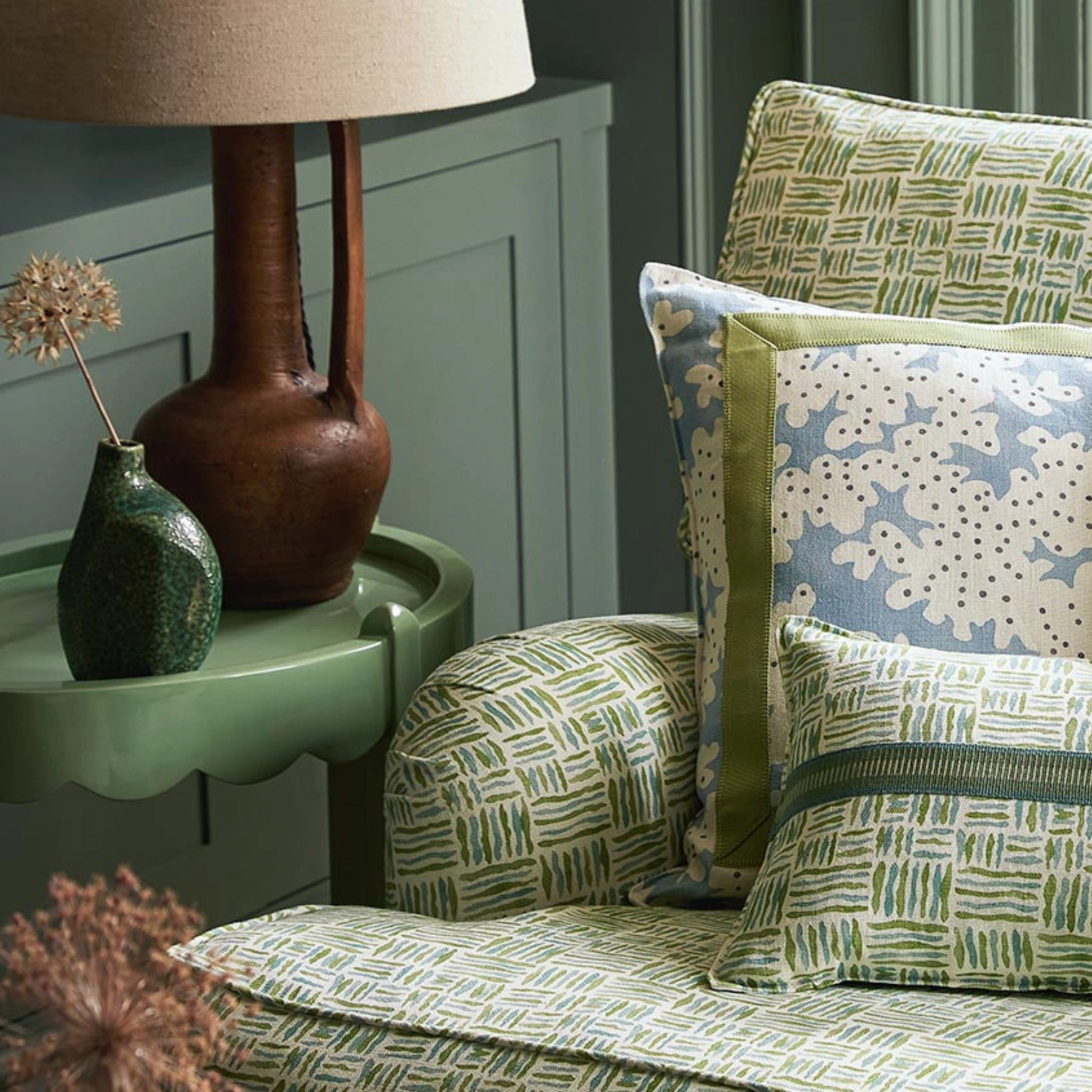 An armchair upholstered in a green fabric, sitting next to a green side table