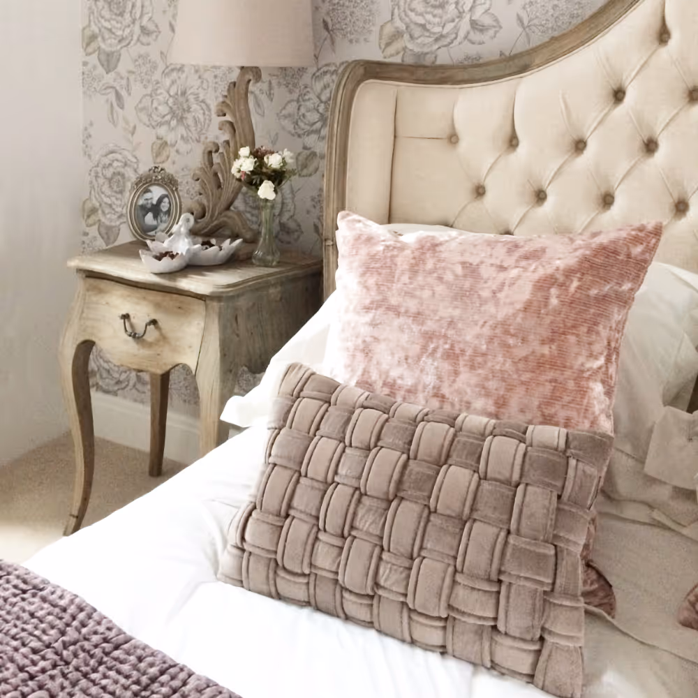 A romantic bed with a French style upholstered bed, elegant oak bedsides and blush pink velvet cushions.