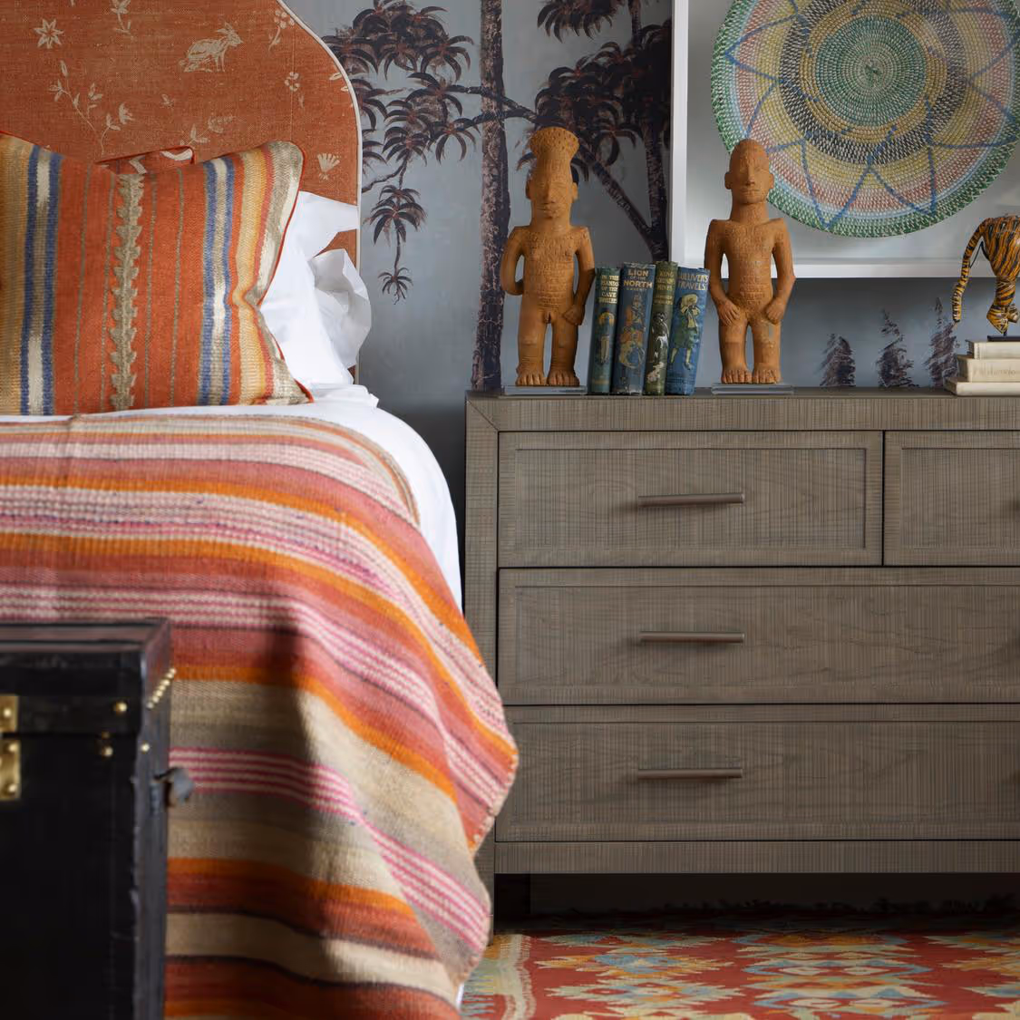 A ethnic styled bedroom with large chest of drawers and a kilim style bed throw.
