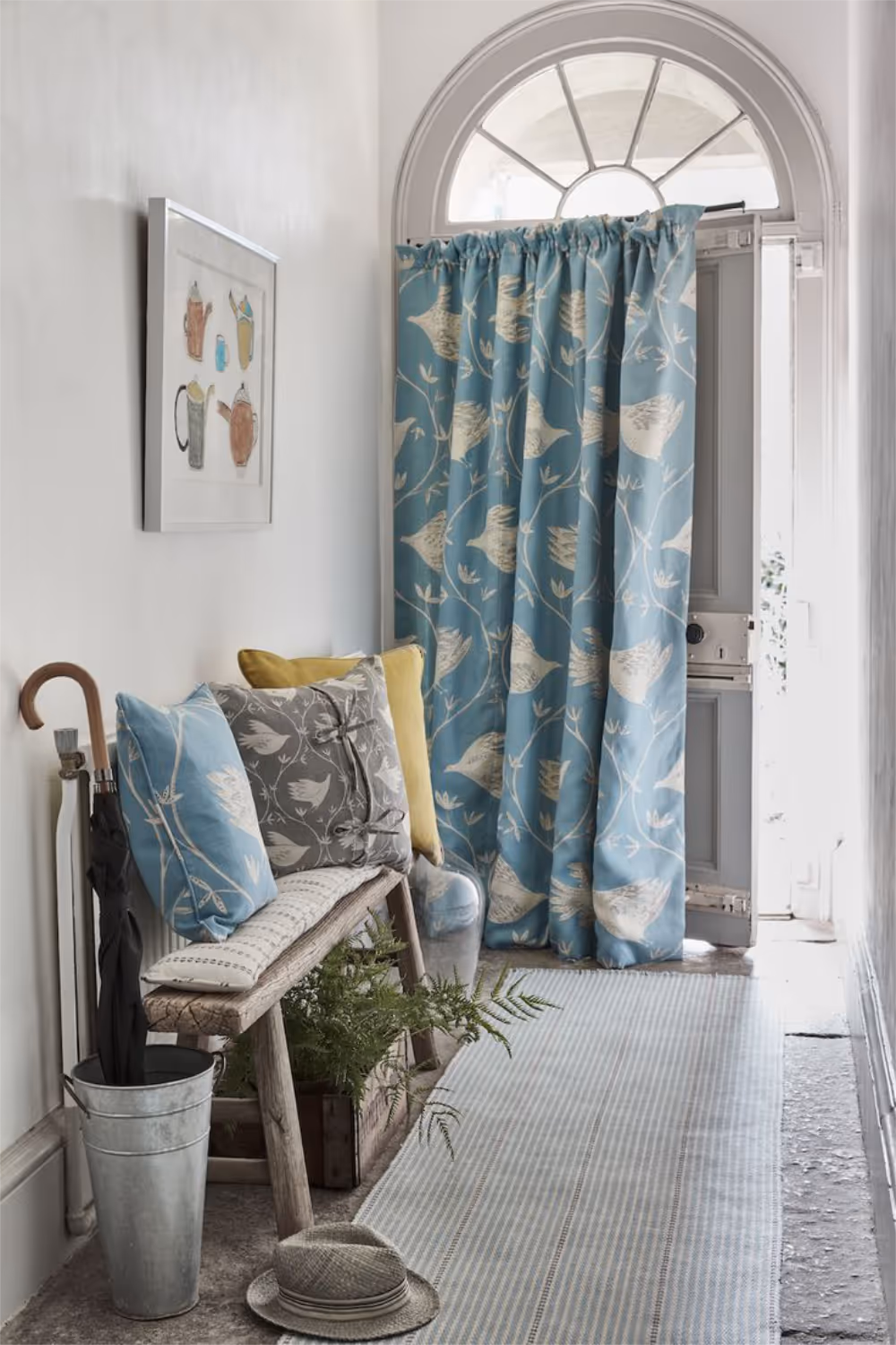 A white painted hallway with a rustic wooden bench and a curtain across the front door made from blue printed linen.