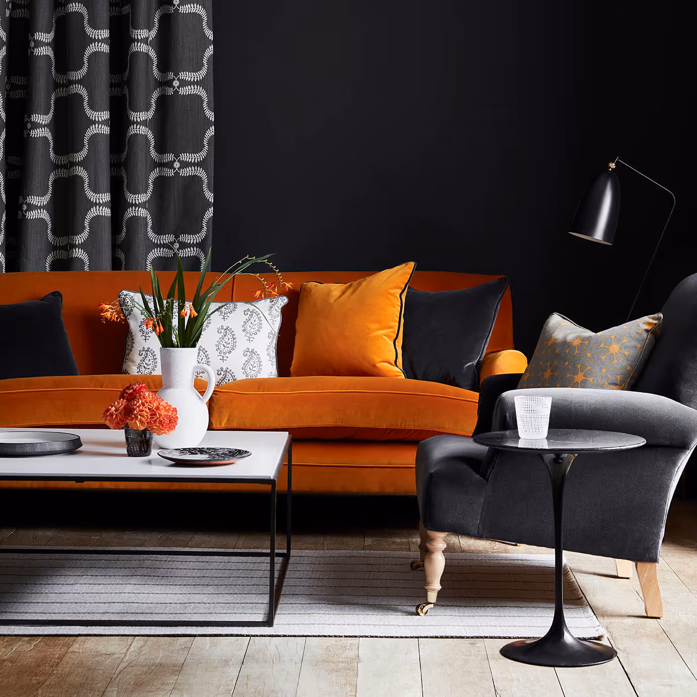 A black living room with an orange velvet sofa and grey velvet armchair.
