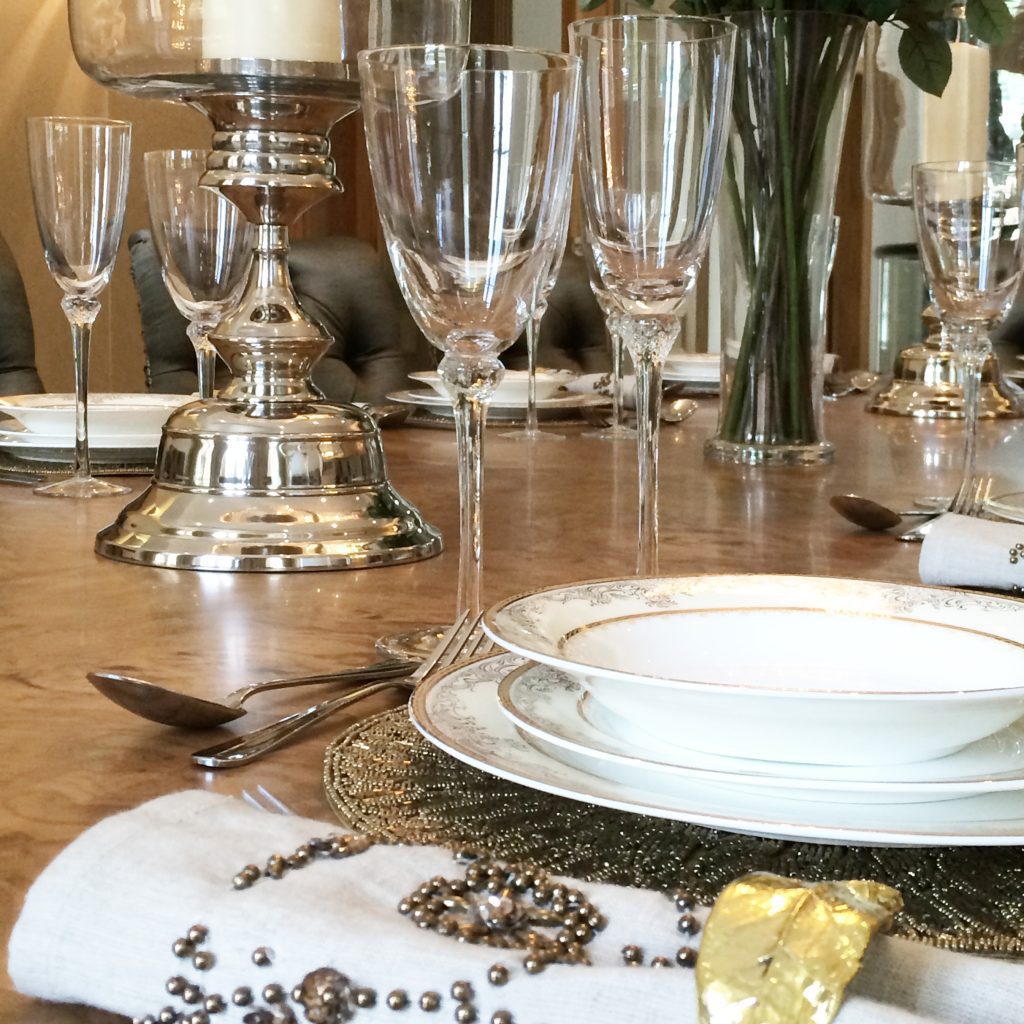 Close up of a dining table laid with gold china and beaded placemats and fine glassware