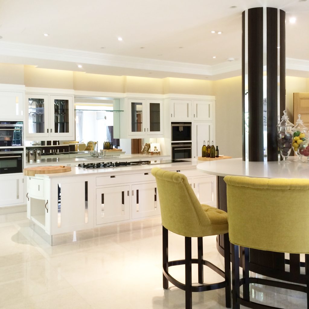 A high-end kitchen in white with mirrored details, and a breakfast bar with green bar stools