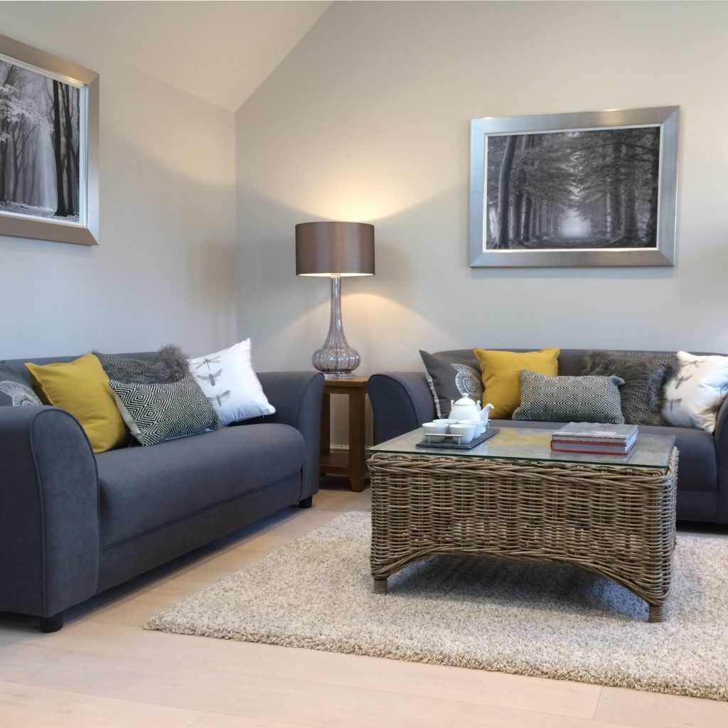 Living room with vaulted ceiling, dark grey sofas with driftwood furniture and ochre cushions