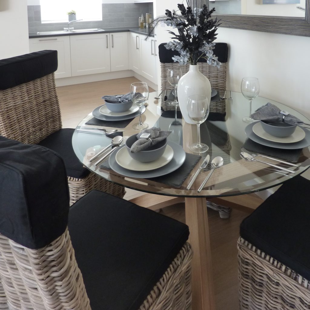 Oak and glass dining table with wicker chairs a in a coastal themed apartment.