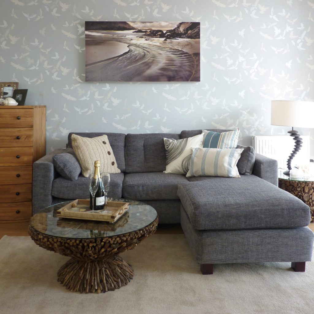 Coastal themed living room with driftwood coffee table, a grey corner sofa, and a seagull pattern wallpaper