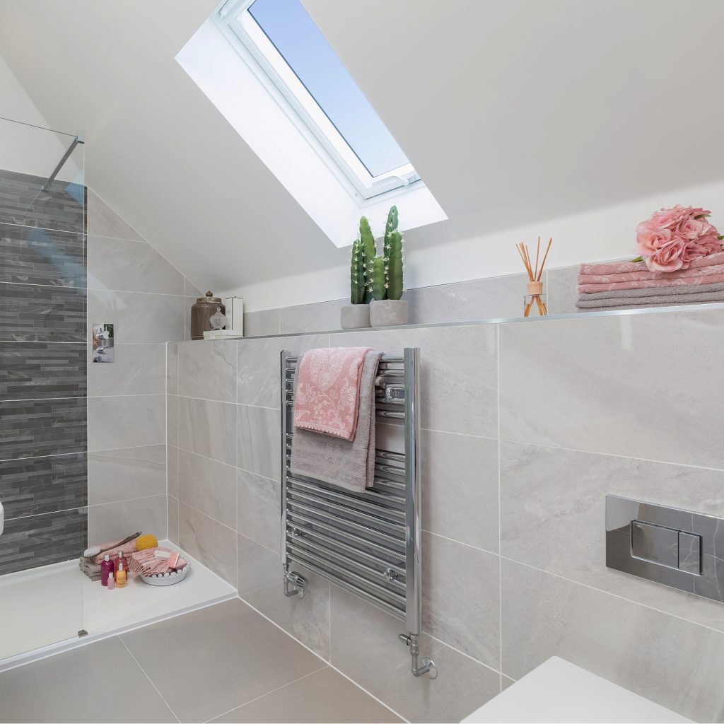 An ensuite shower room with grey tiles and pink towels.