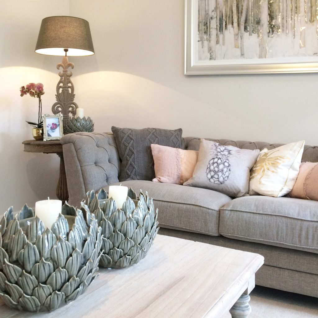 A calm and cosy living room with a grey sofa and layers of blush and charcoal cushions