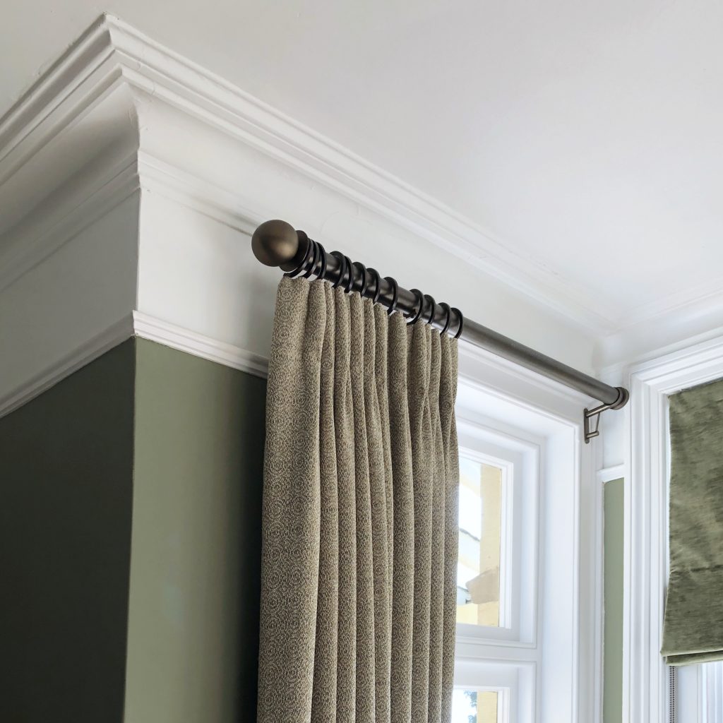 Interlined curtains in a olive green wool fabric, on a bronze curtain pole