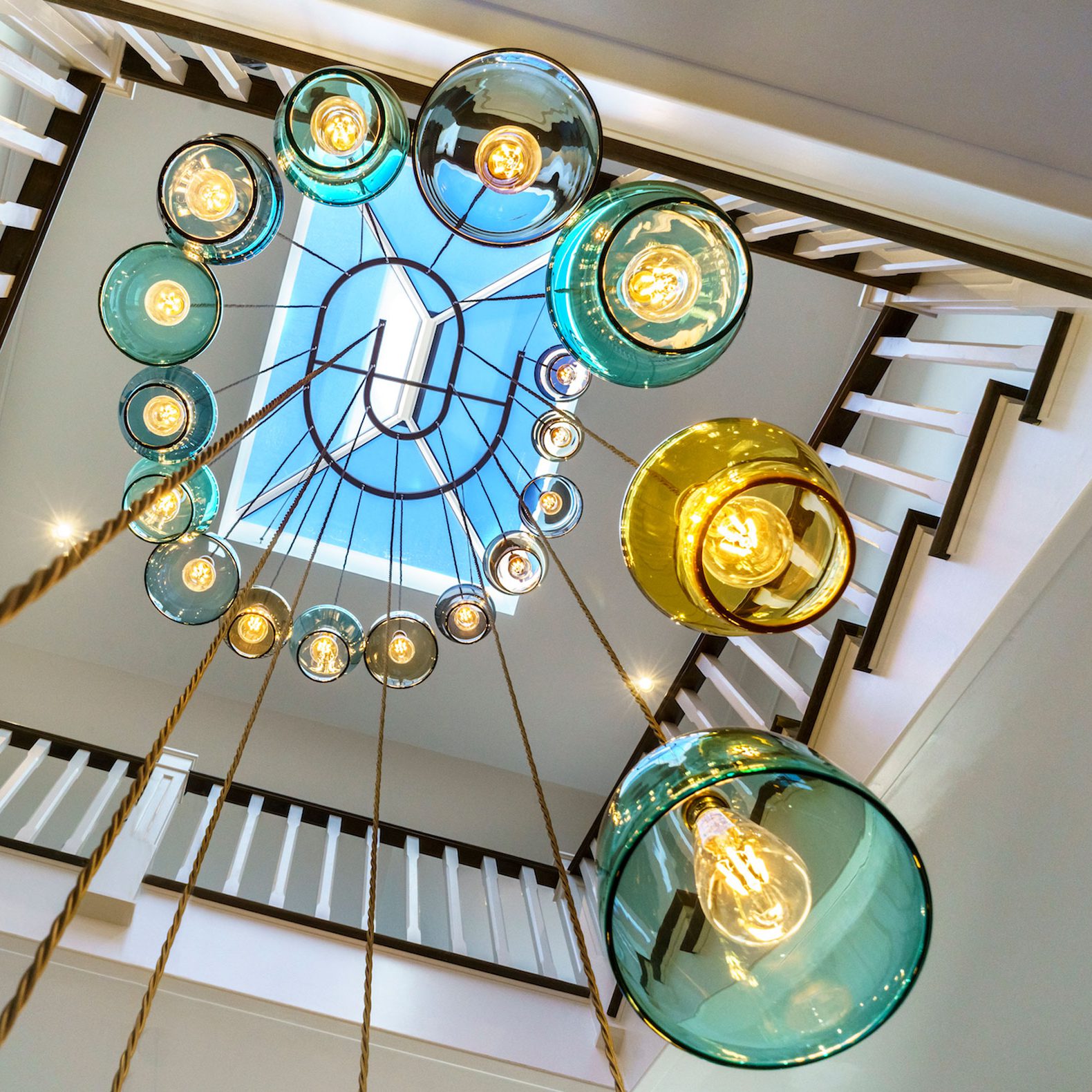 A tall stairwell with handmade spiral pendant made from turquoise and amber hand blown glass.