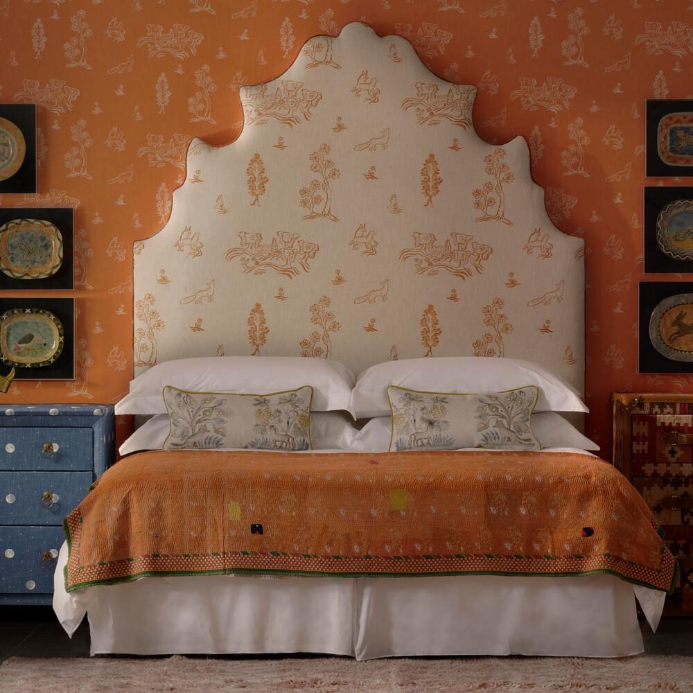 An orange painted bedroom with blue bedsides and a tall upholstered headboard.