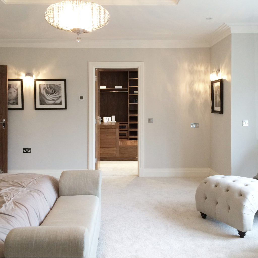 A neutrally decorated bedroom, looking through doorway into walnut dressing room beyond