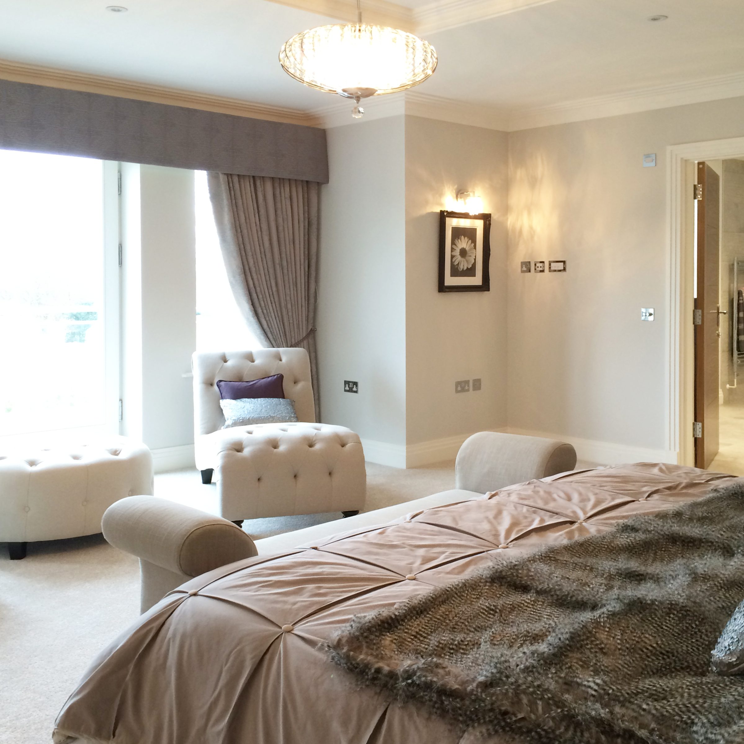 Large bedroom decorated in neutral hues with cushions and throws in antique mauve and dusky pink