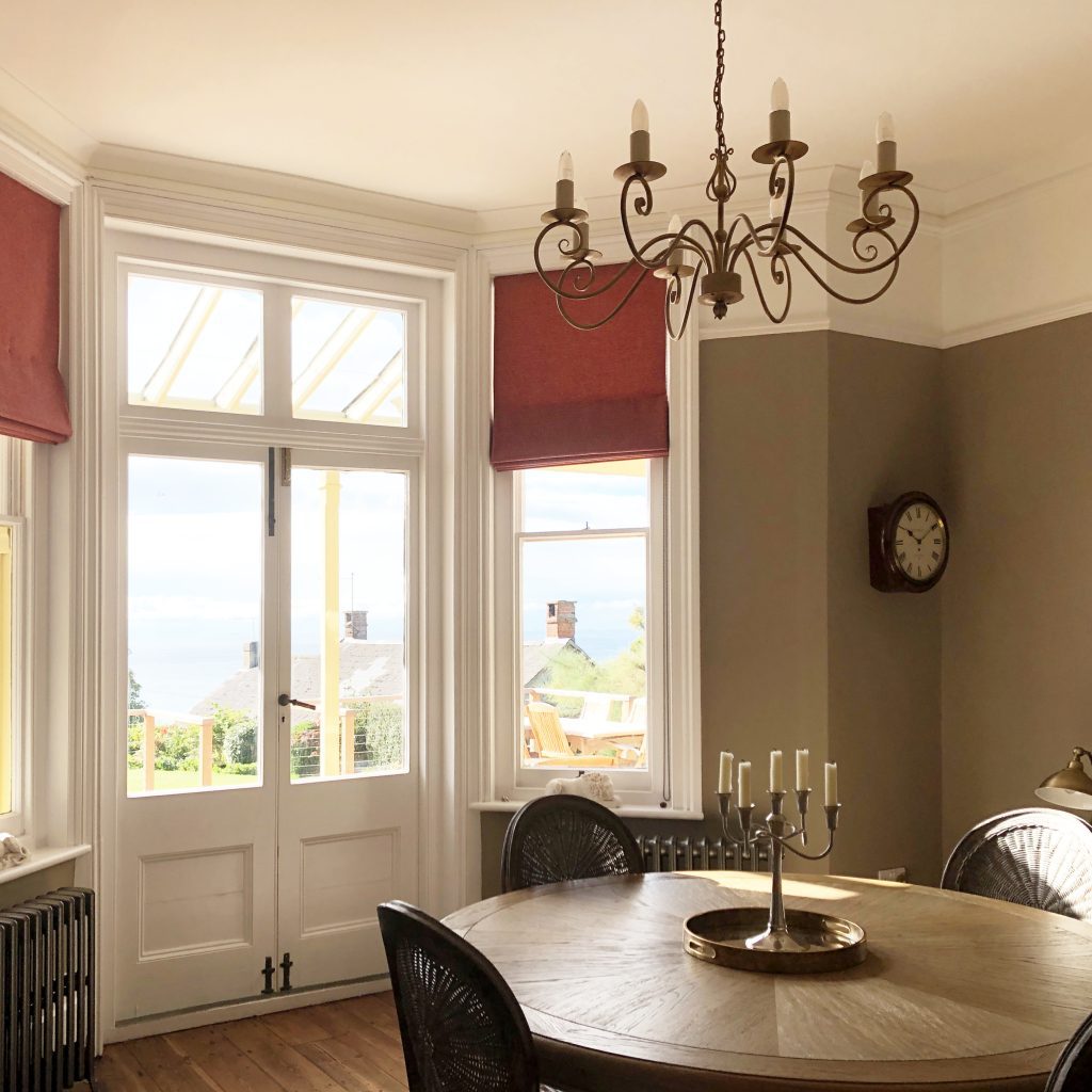 Taupe dining room with red wool roman blinds and grey oak dining table