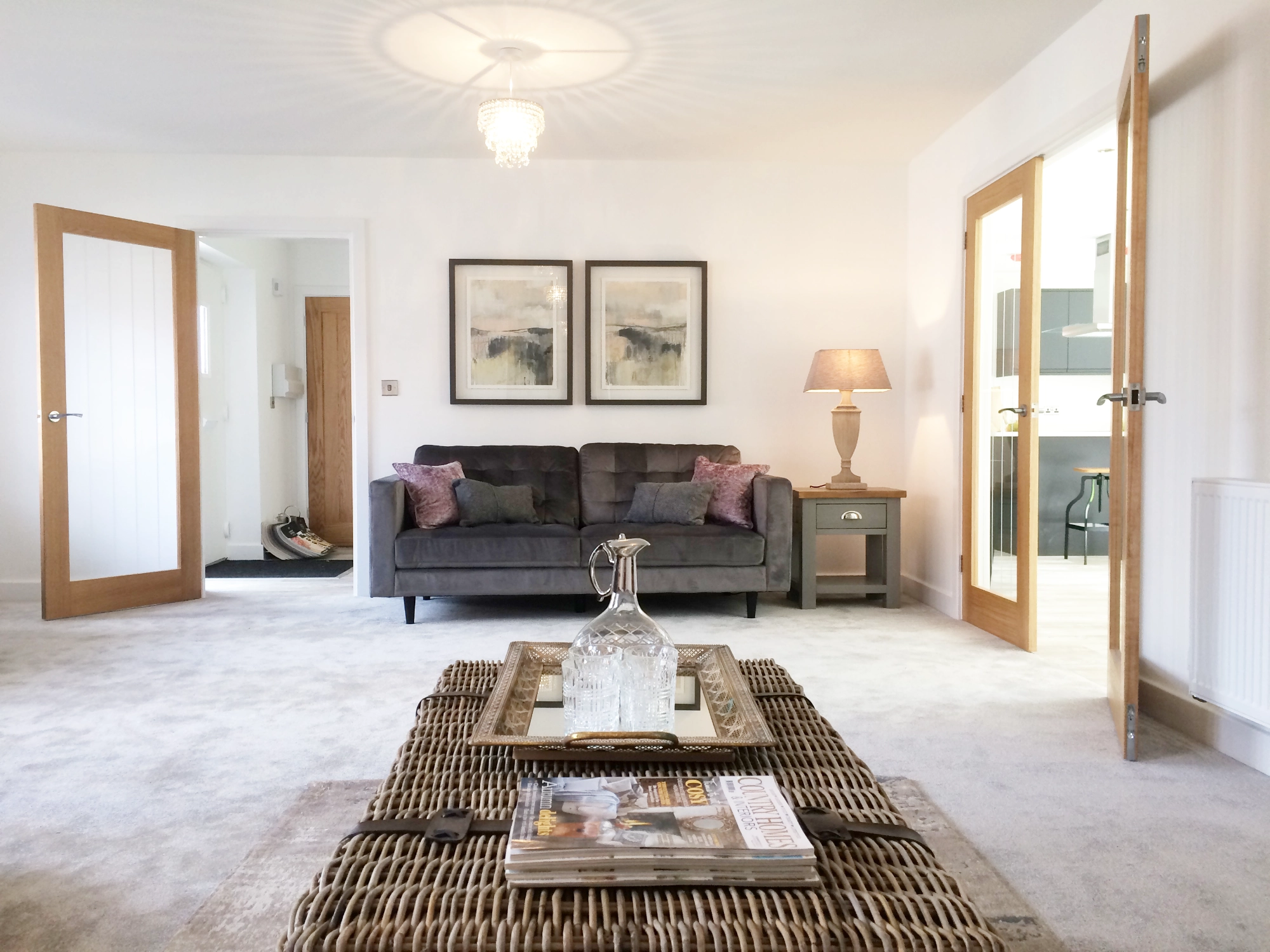 A living room with a wicker coffee table and a grey velvet sofa with pink accent cushions