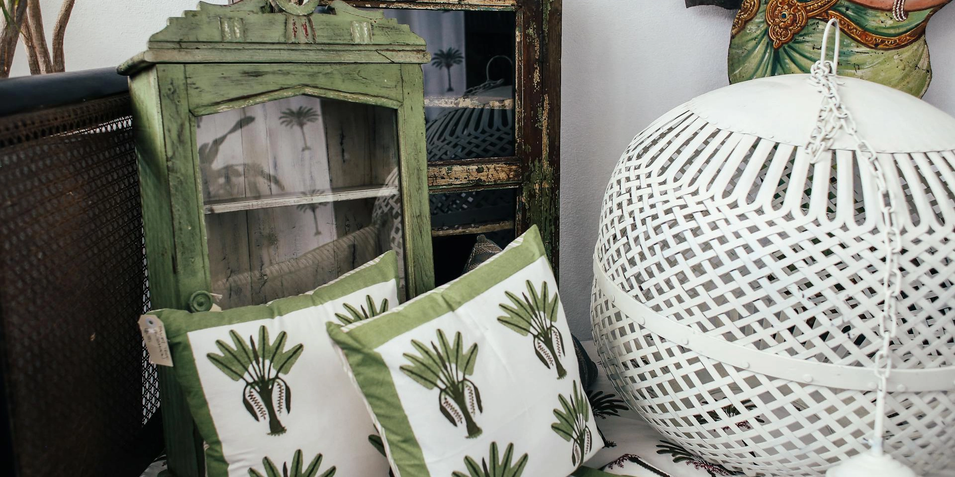 A display of some cushions, an old green cupboard and a rattan lantern