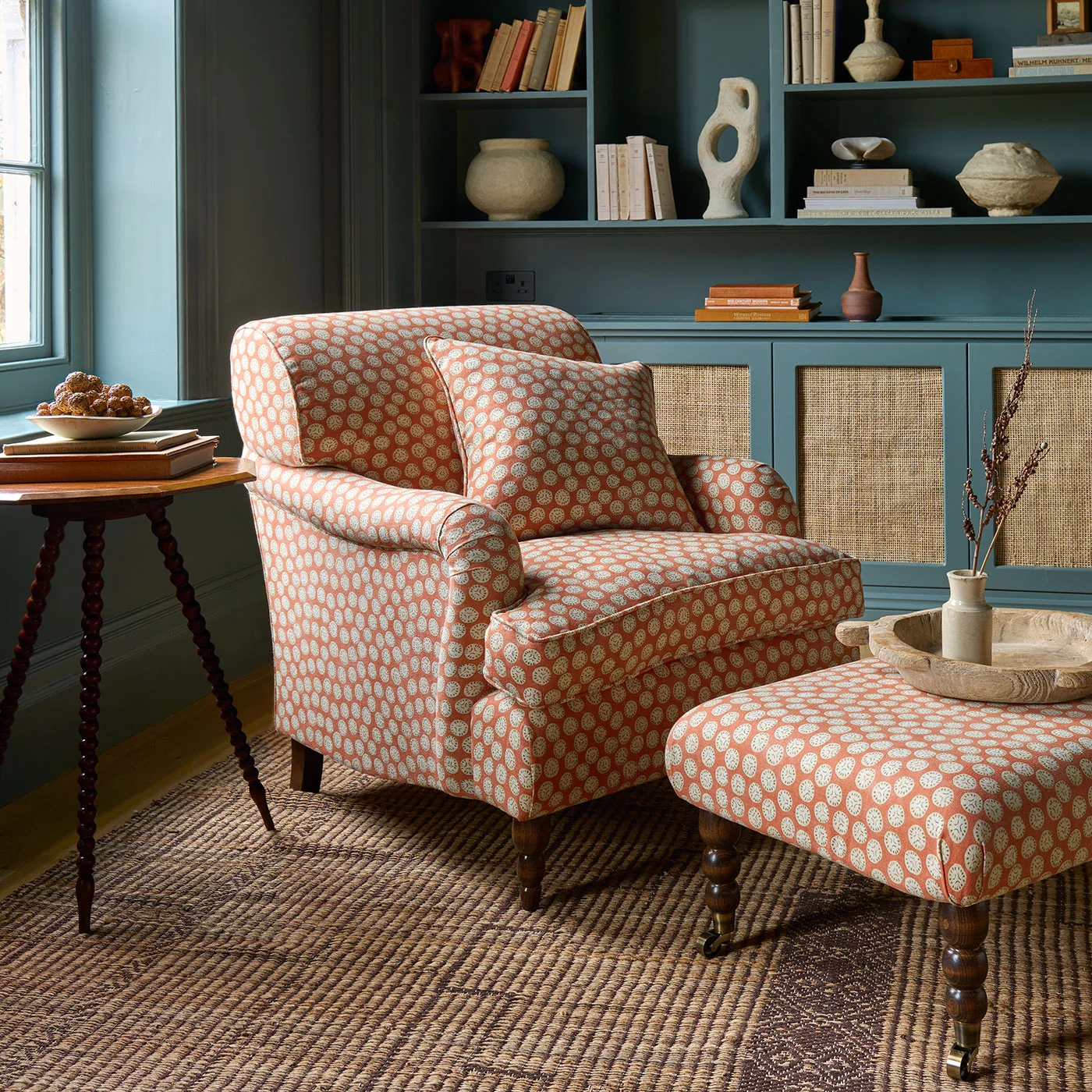 An old armchair upholstered in an orange print, sat in front of a teal green wall