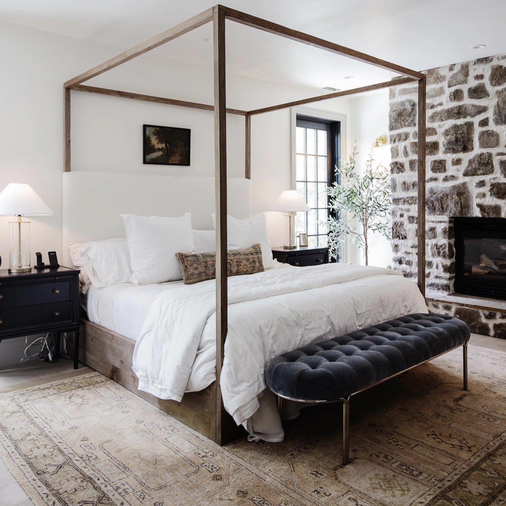 A modern country styled bedroom with a natural stone wall and a mix of antique and modern furniture