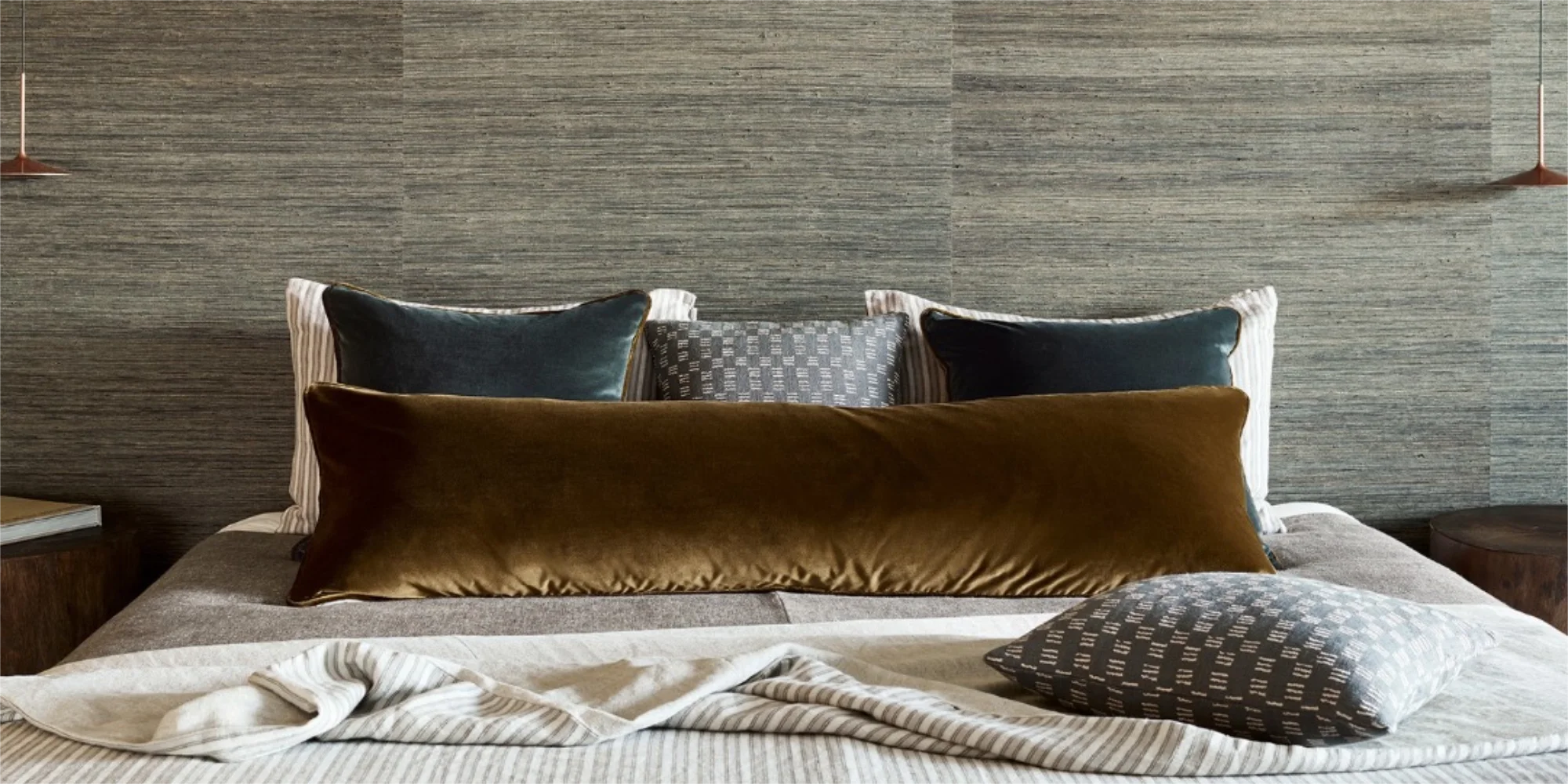 A bedroom with seagrass wallpaper and velvet cushions on the bed