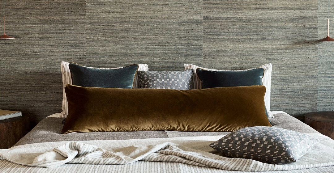 A masculine feeling bedroom with velvet cushions and a grasscloth wallcovering