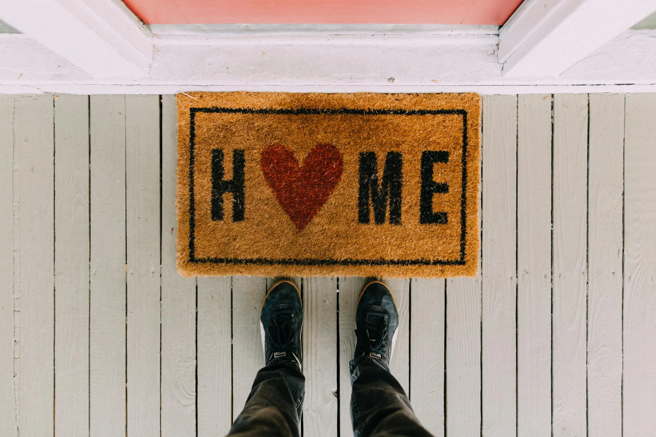 A person stood before a doormat at the entrance to a house