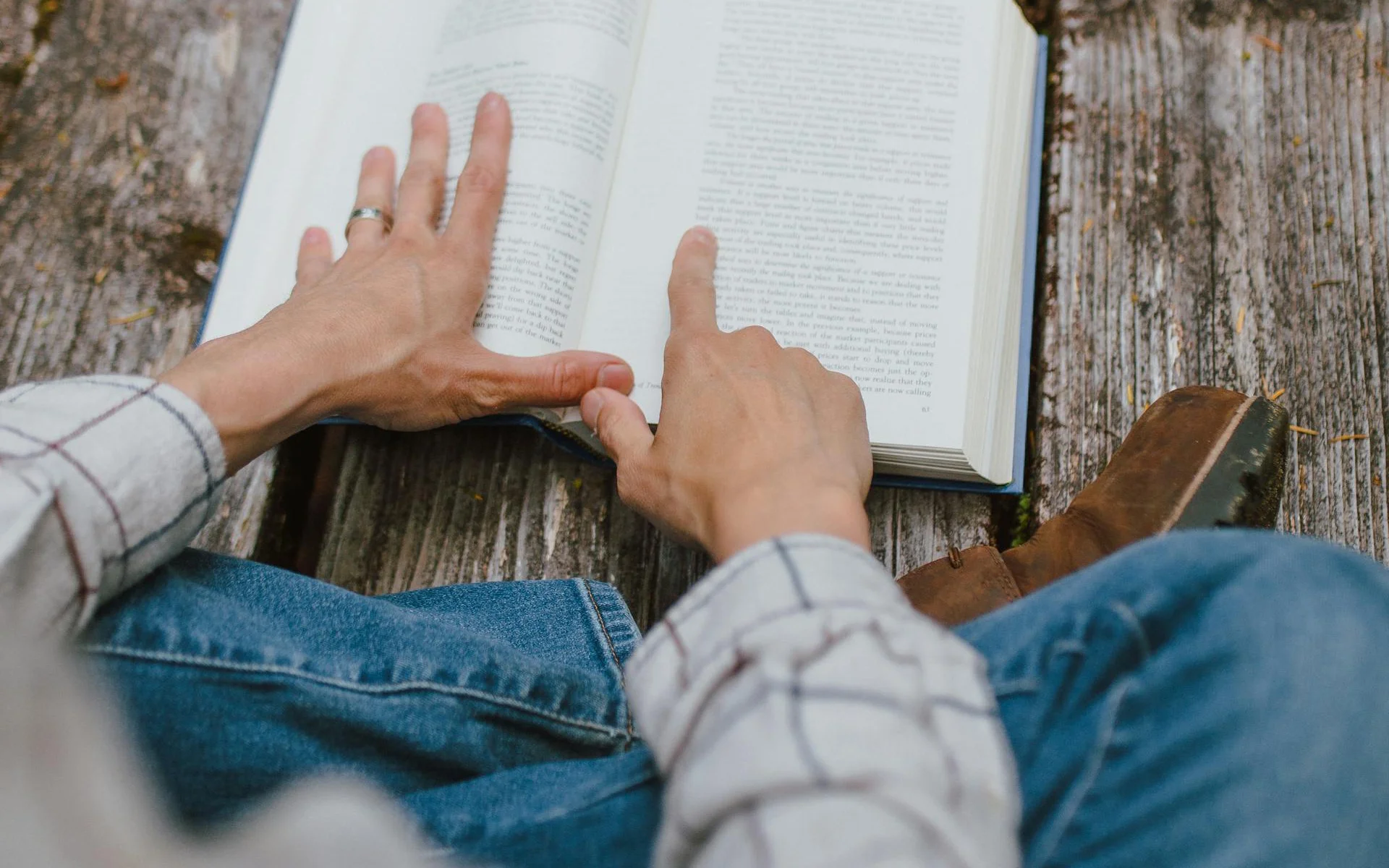 A person sitting on wooden decking reading a book